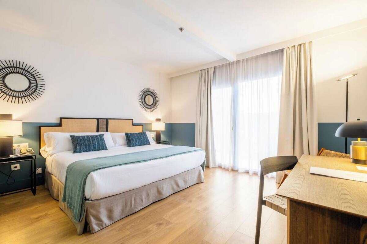 A hotel room with a bed, bedside tables, a desk, and a chair.