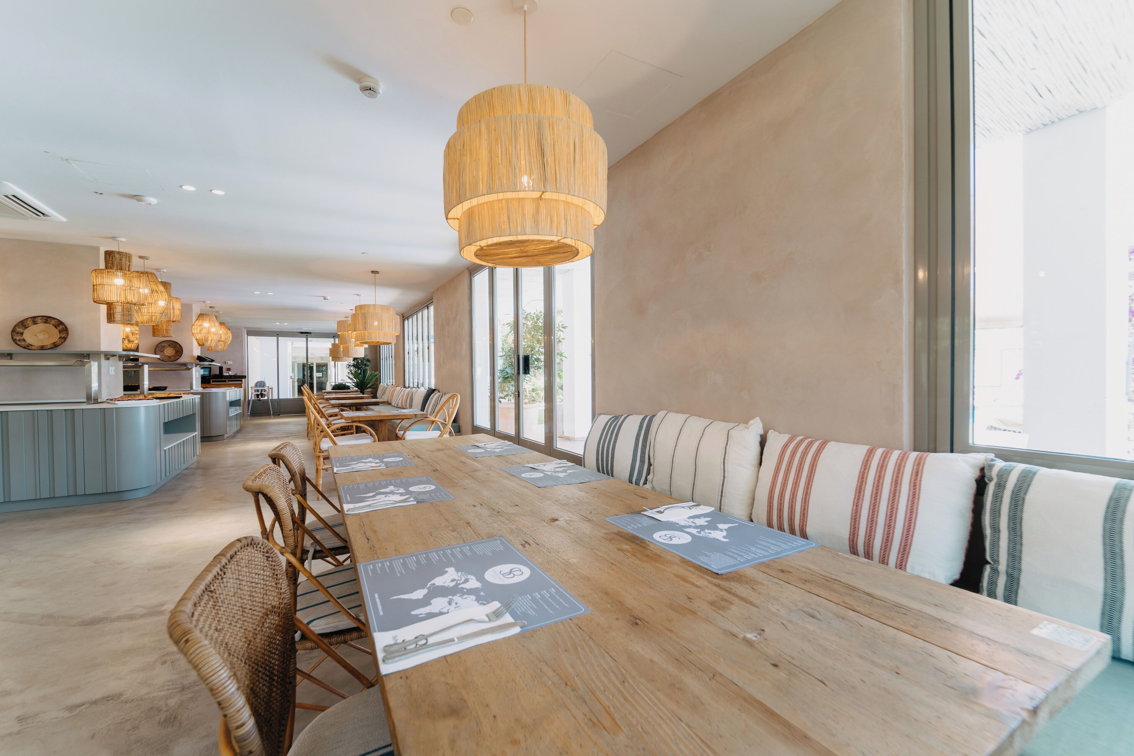 A modern dining area with a long wooden table, wicker chairs, and a central island with a kitchen counter.