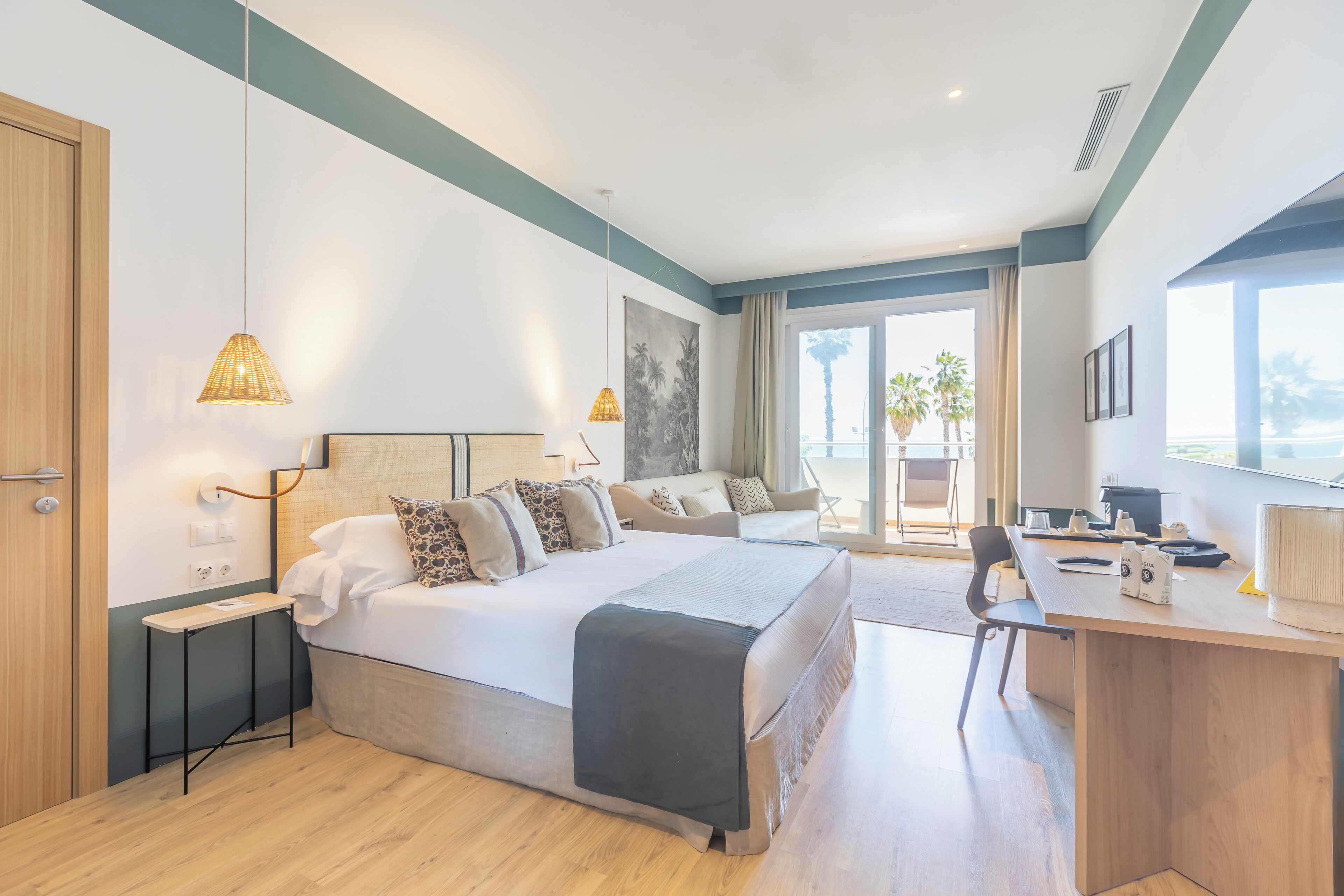A modern hotel room with a large bed, a desk, and a balcony with a view.