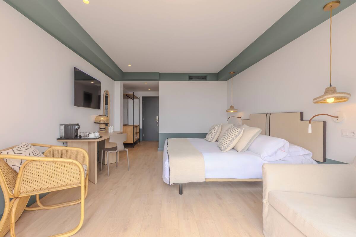 A modern hotel room with a bed, a desk, a chair, and a sofa.