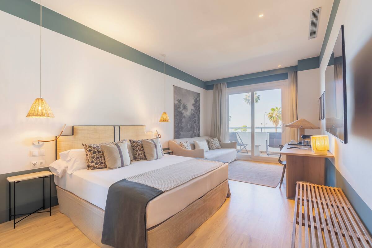 A modern hotel room with a large bed, a desk, and a balcony with a view.