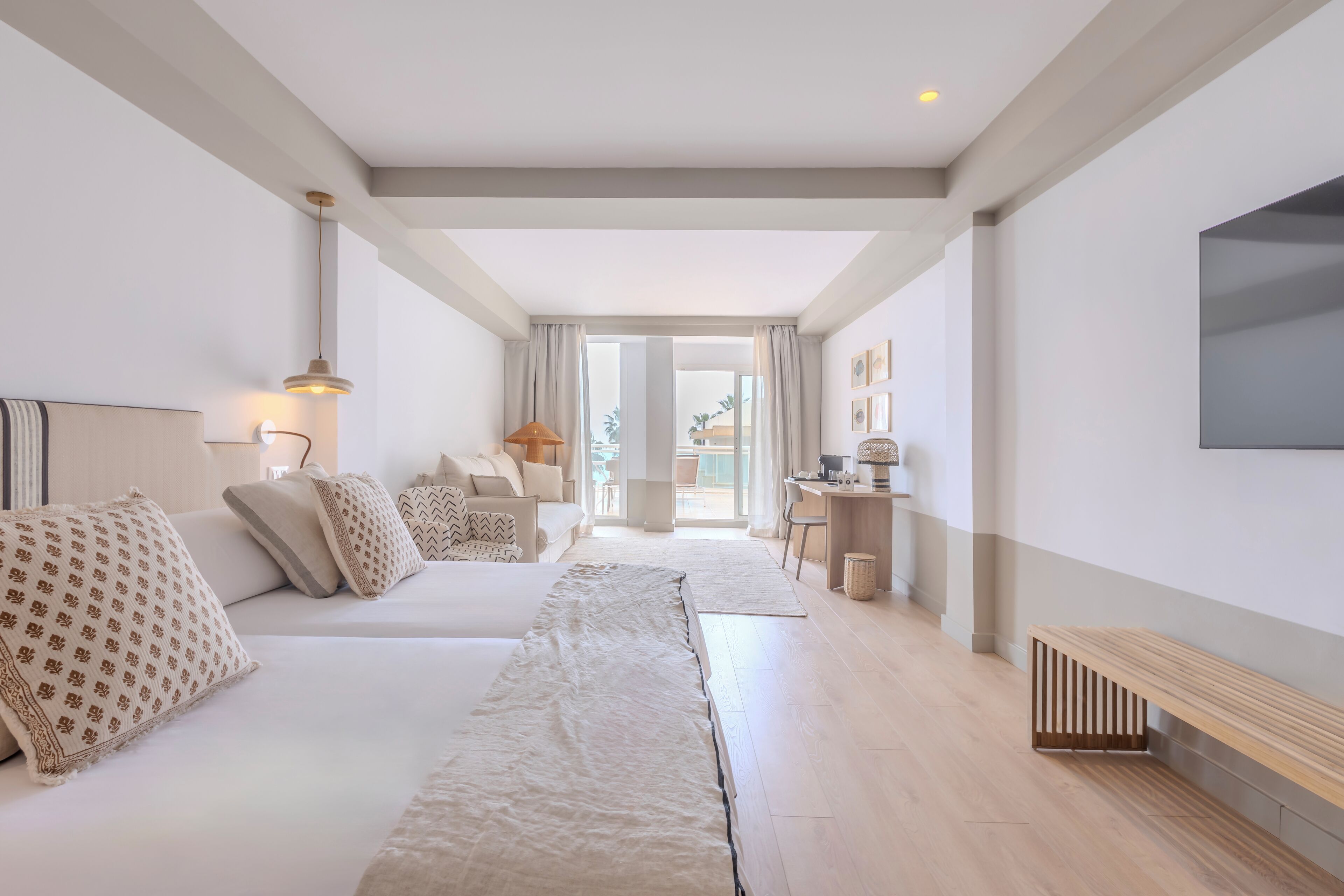 Moderni hotellihuone, jossa on pitkä sohva, työpöytä ja suuri ikkuna.