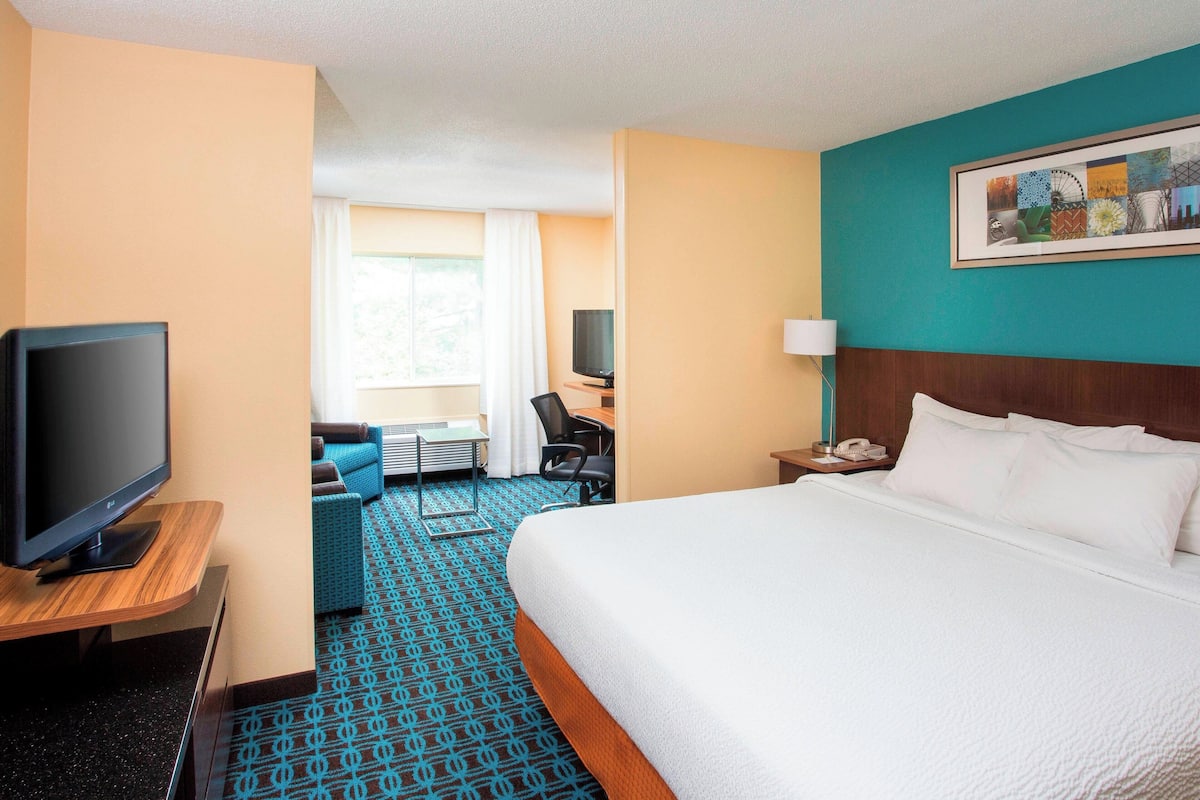 A hotel room with a large bed, a television, a desk with a chair, and a window with curtains.