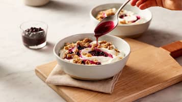 Een kom yoghurt met granola en bessen op een houten plank.