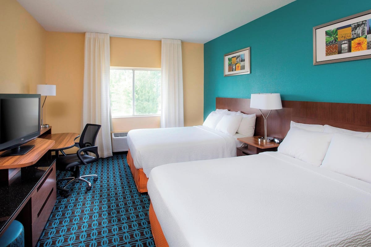 A hotel room with two beds, a desk with a TV, a chair, and a window with curtains.
