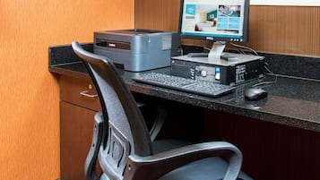Una oficina de hotel con una computadora de escritorio, una impresora y un teclado sobre un escritorio negro.