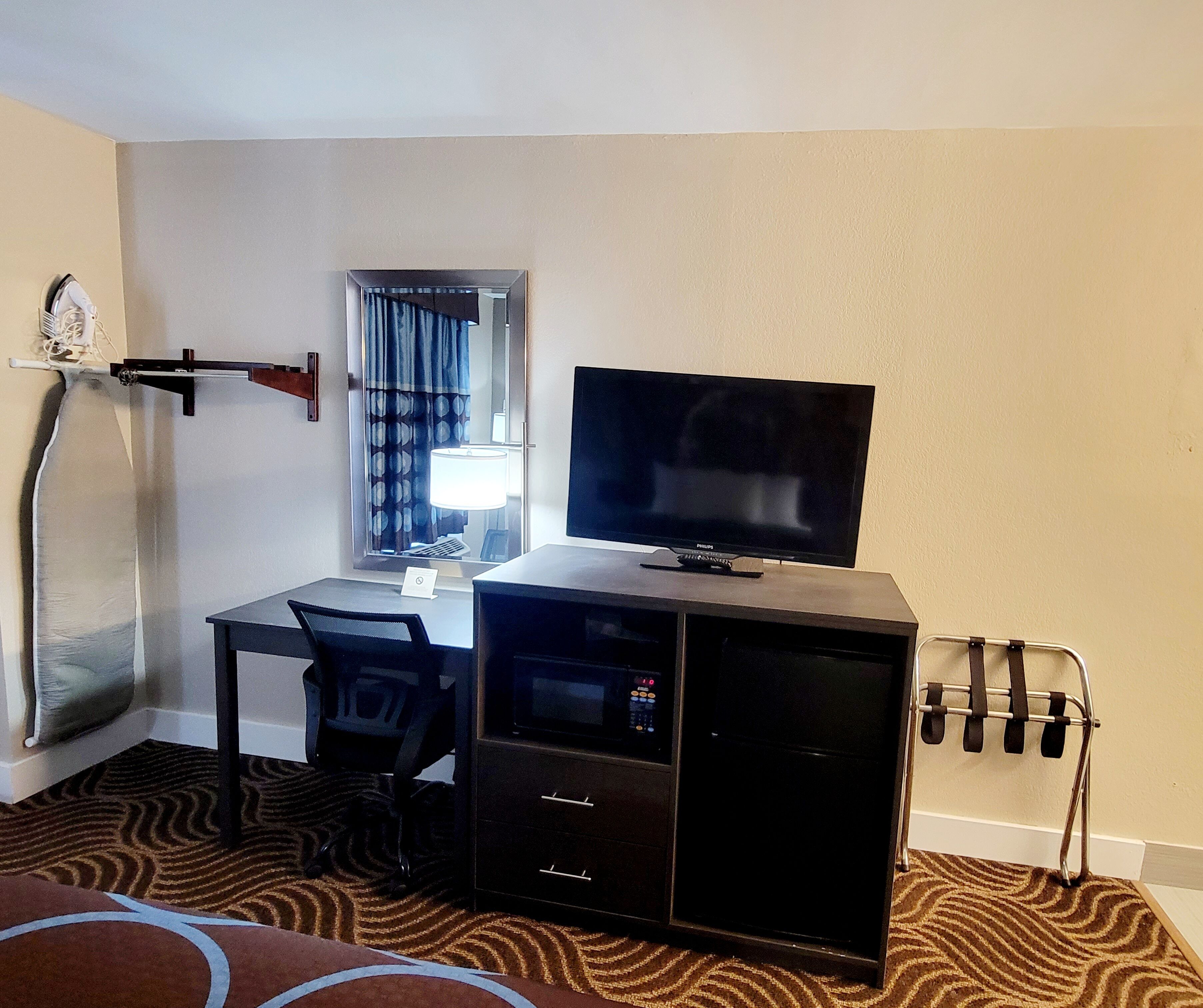 A hotel room with a desk, chair, television, and a microwave.