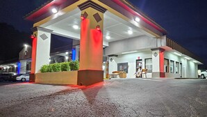 Una estación de servicio de noche con marquesina, surtidores de combustible y algunos coches aparcados.