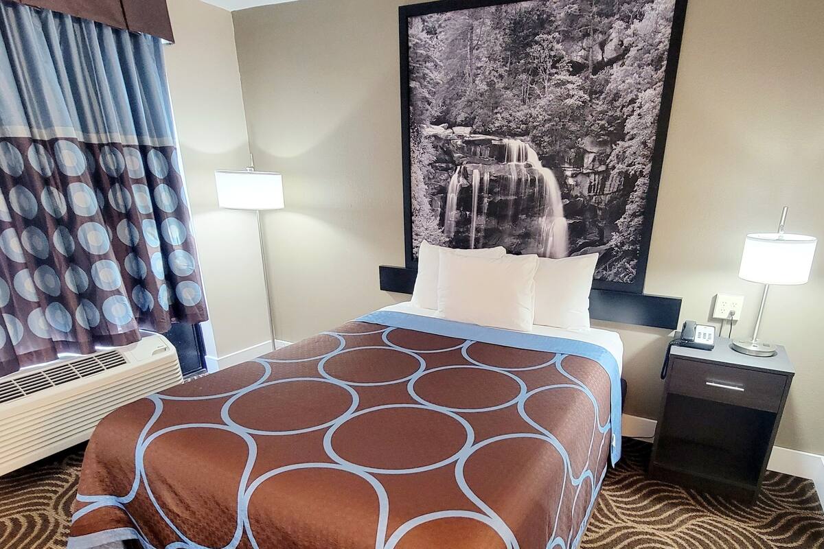 Habitación de hotel con cama, mesita de noche, lámpara, calefactor y un cuadro grande en la pared.