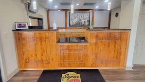 Un mostrador de recepción con paneles de madera, un cartel de bienvenida enmarcado y una alfombra negra con un logotipo.