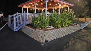 Un mirador con barandilla blanca y base de ladrillo, rodeado de plantas y flores.