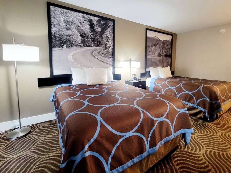 A hotel room with two beds, a large window, and a painting of a road and trees.