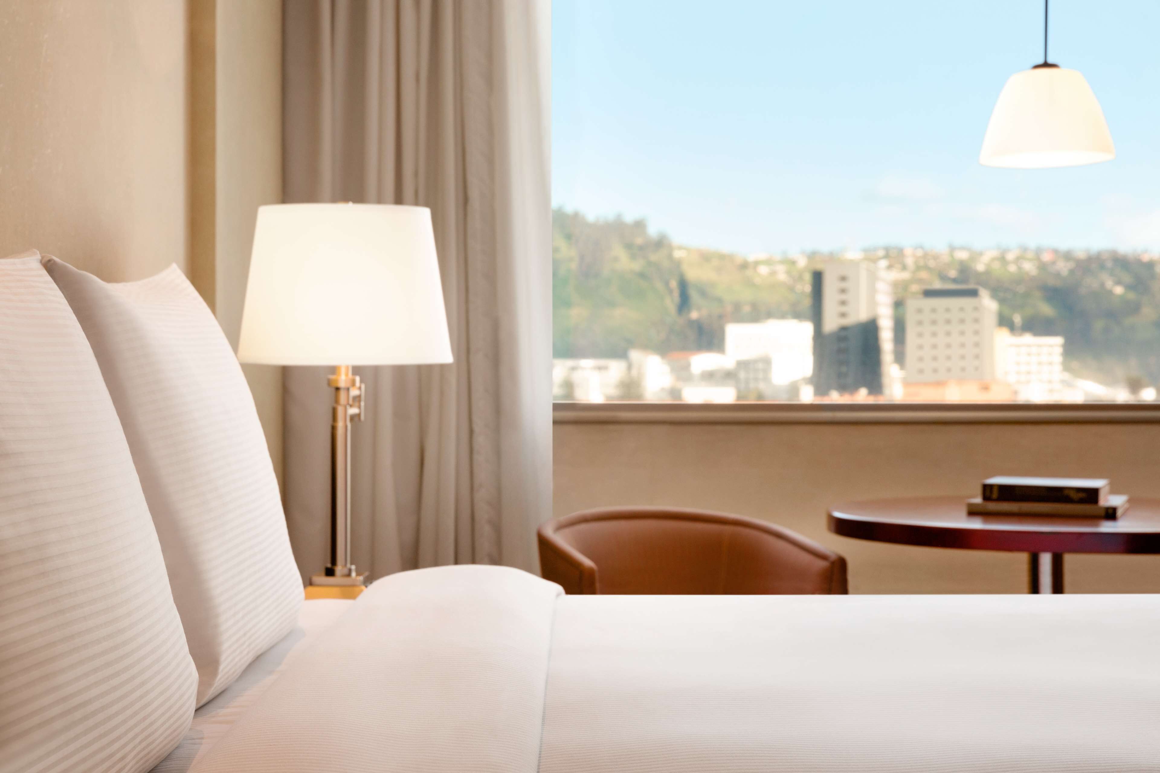A hotel room with a bed, a lamp, a chair, and a table.