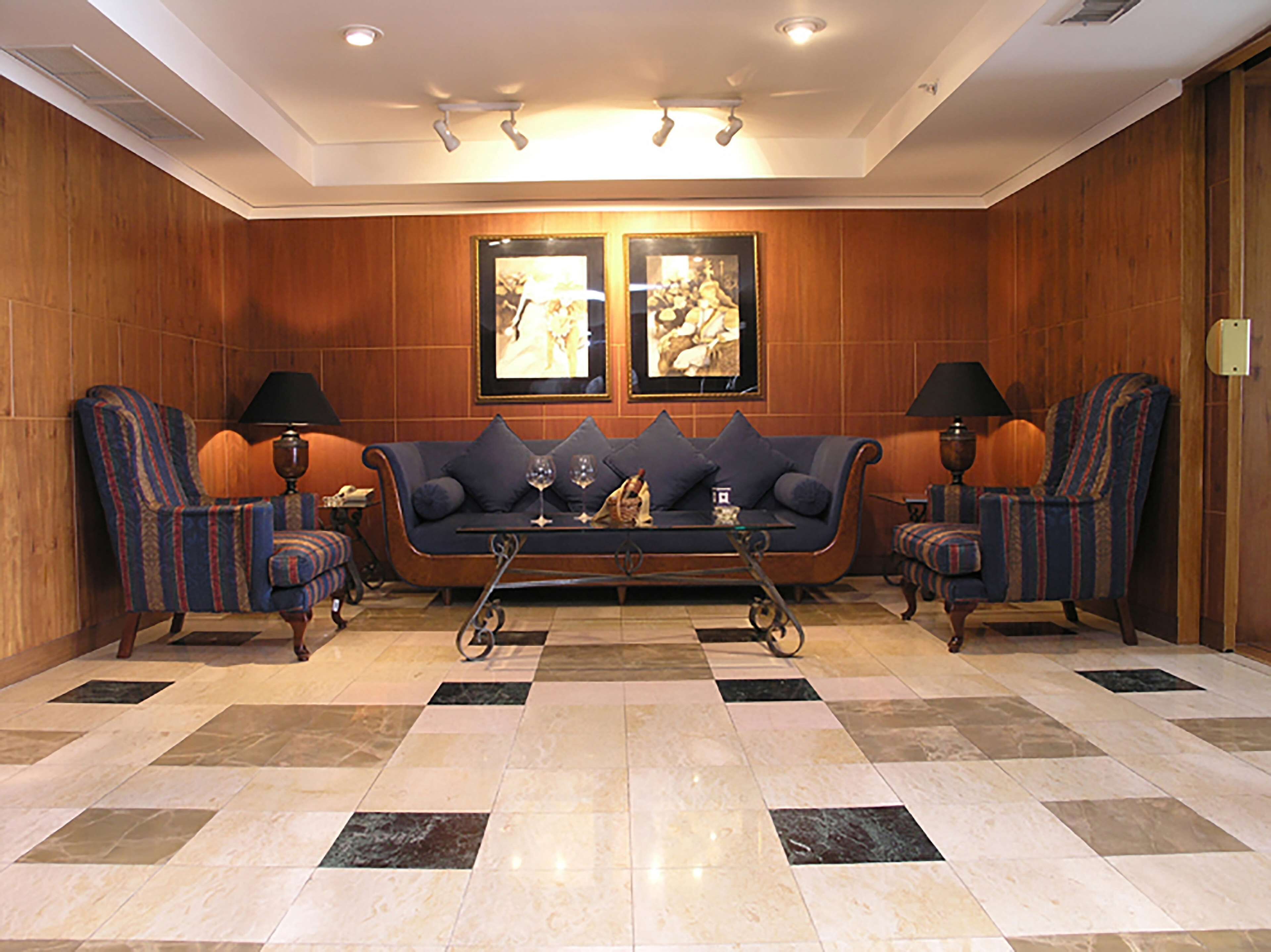 A room with a sofa set, two armchairs, a coffee table, and two framed pictures on the wall.