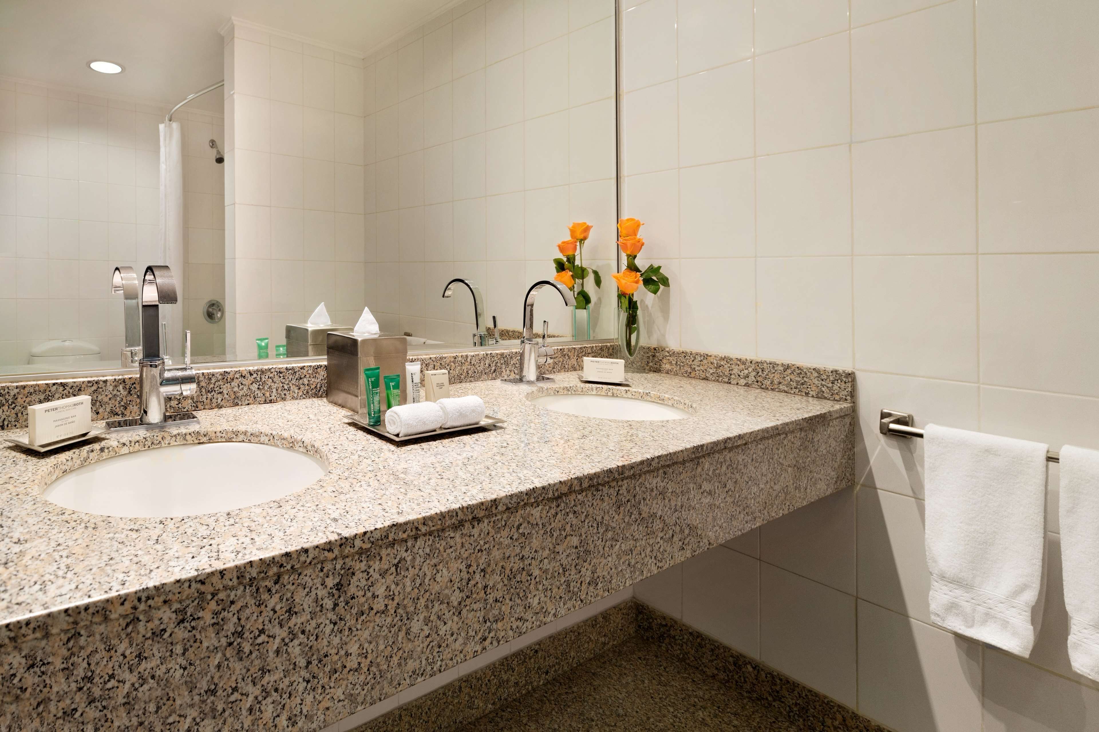 Un baño con dos lavamanos, ducha y perchero para toallas.