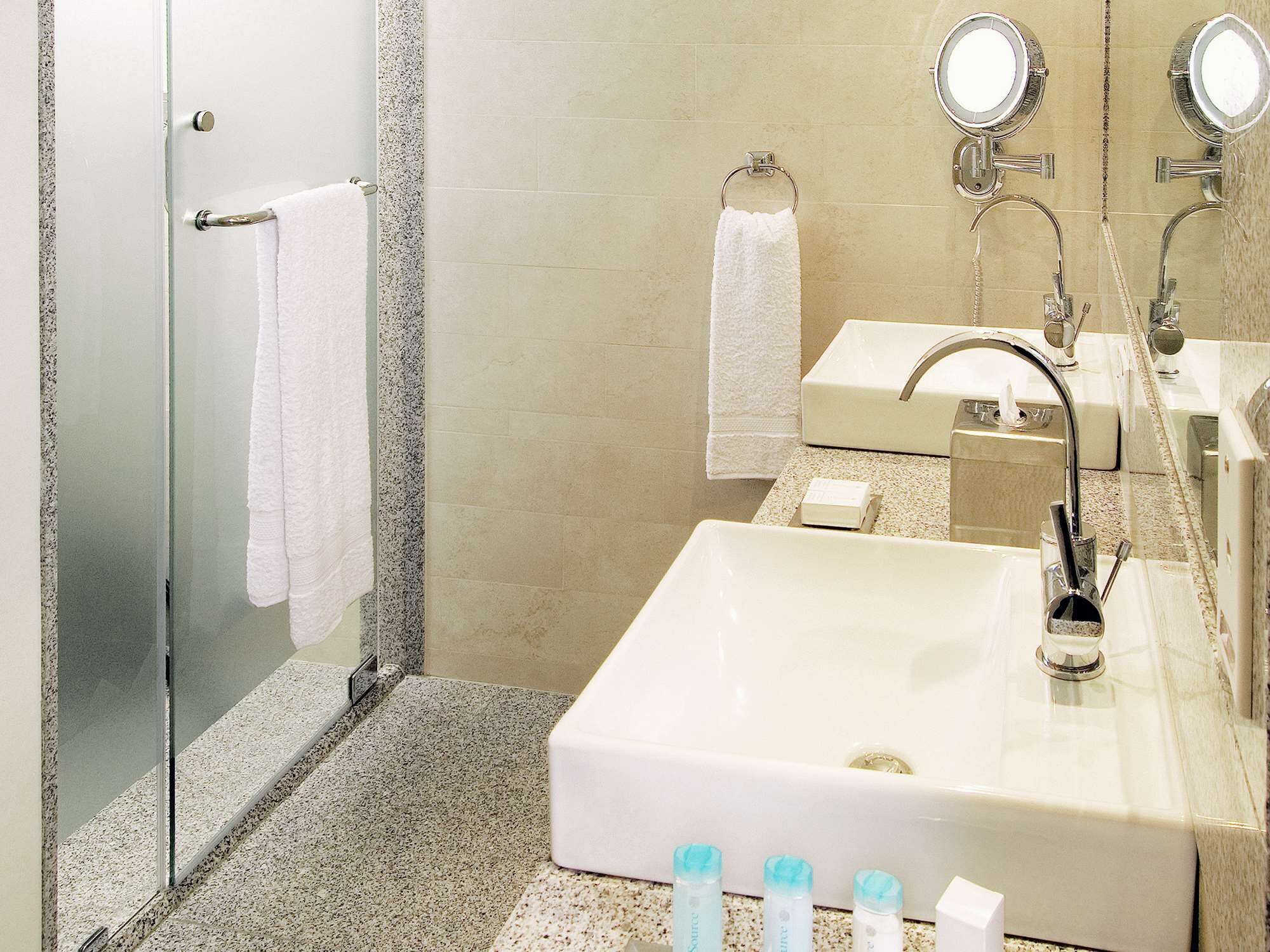 Un baño moderno con cabina de ducha de vidrio, un lavabo blanco con espejo y artículos de aseo en la encimera.
