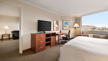 A hotel room with a bed, desk, chair, TV, and city view.