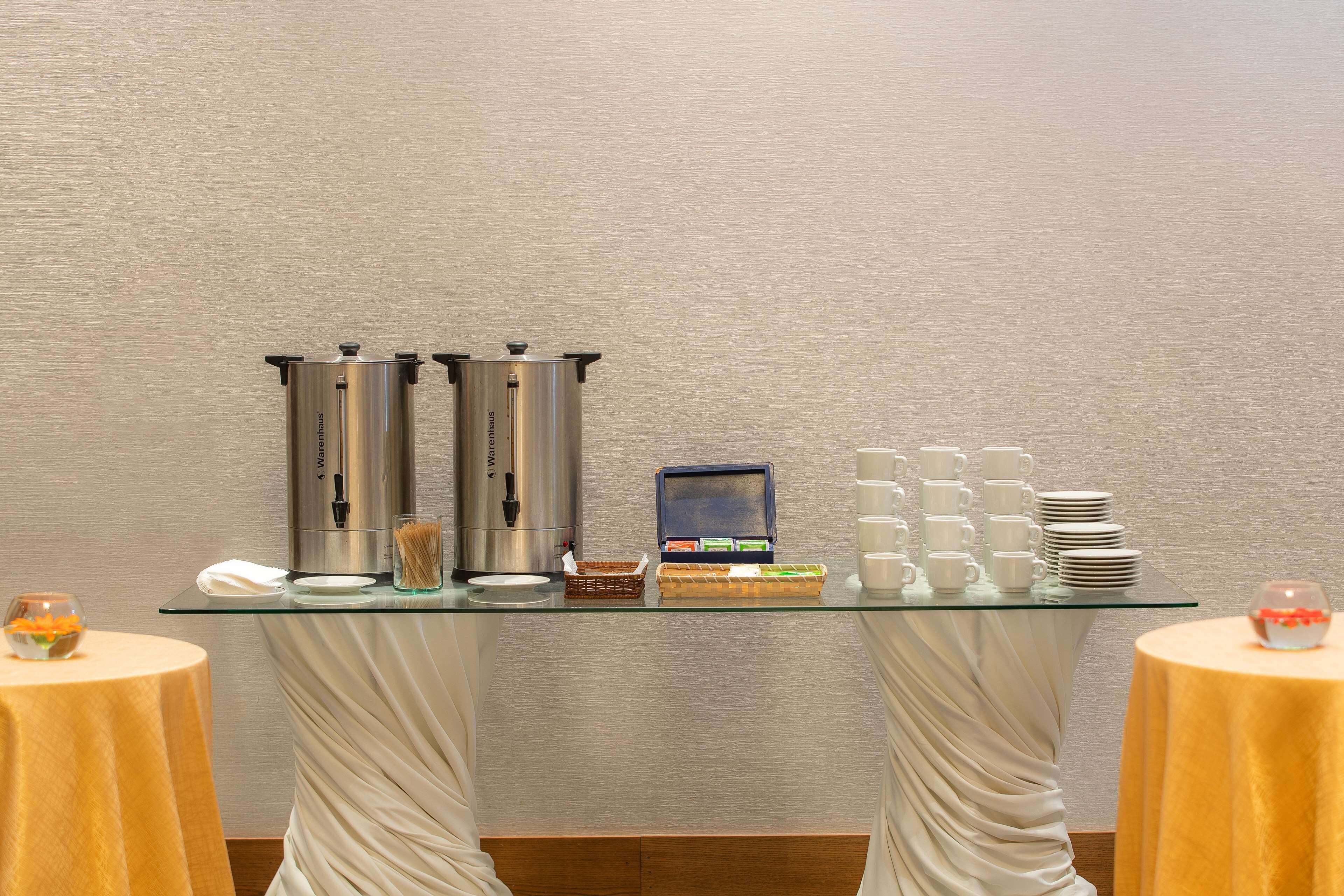 A buffet setup with a coffee station, a small refrigerator, and stacked plates and cups.