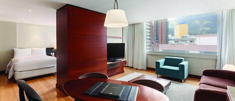 Una habitación de hotel con una cama, un escritorio con una computadora portátil, un televisor y vistas a la ciudad.