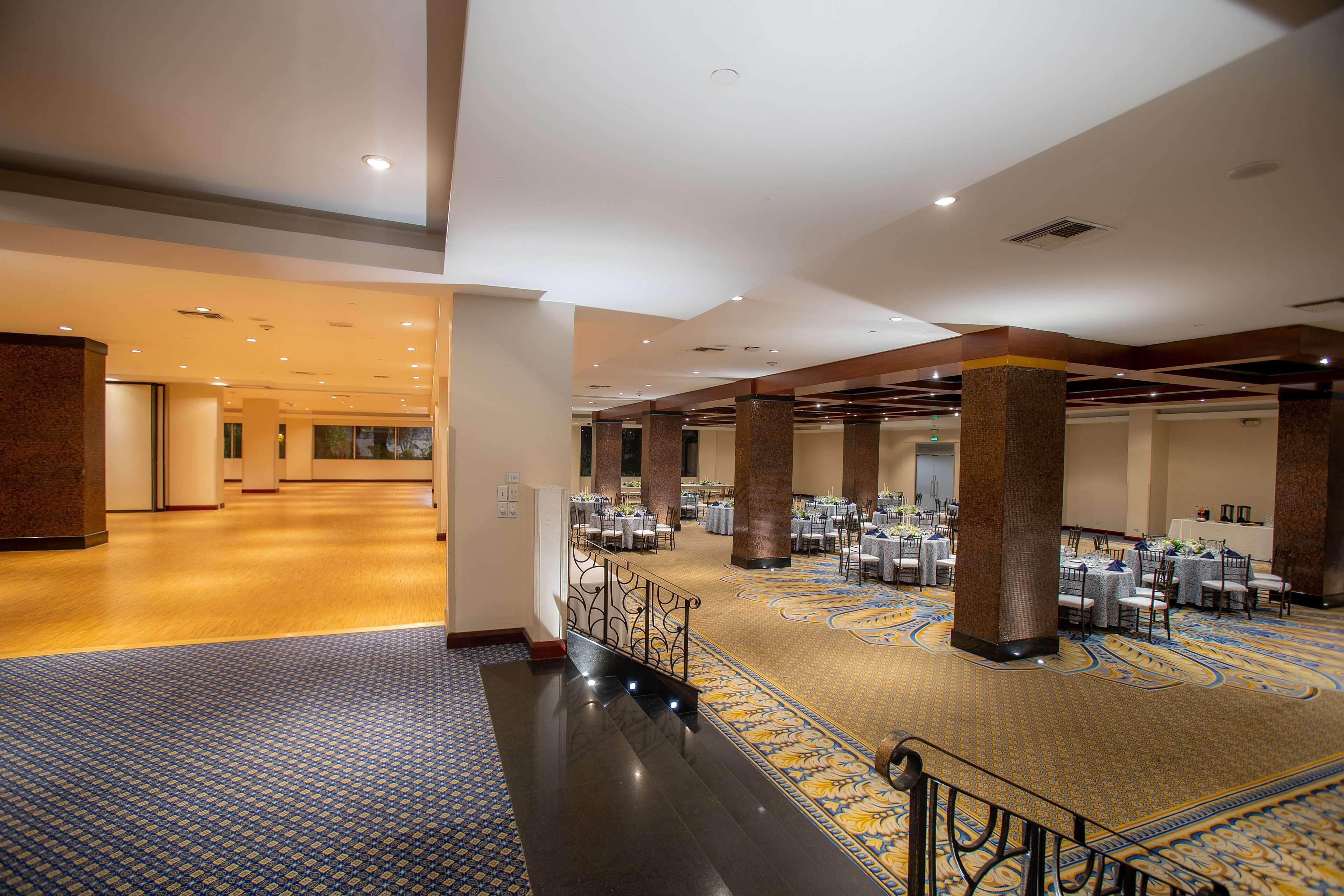 A spacious hotel lobby with a grand staircase, multiple dining areas, and a patterned carpet.