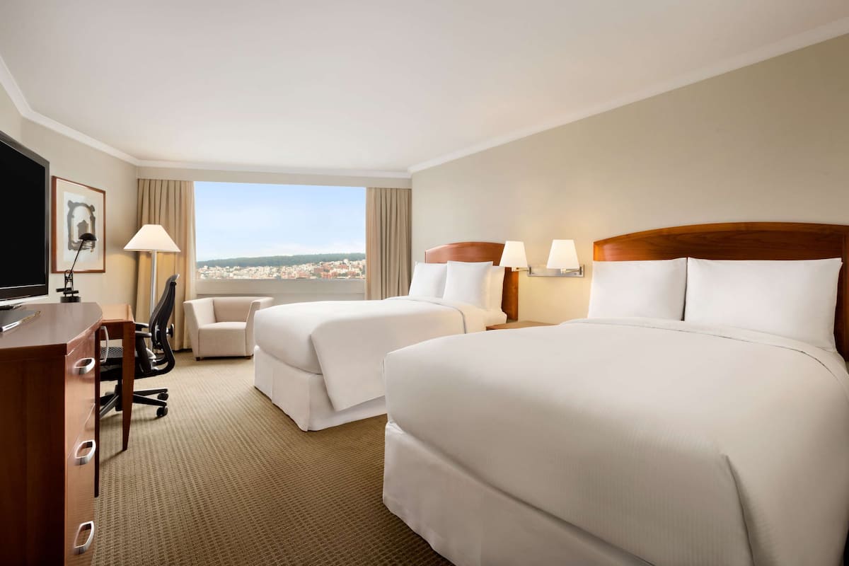 A hotel room with two beds, a desk, a chair, and a TV.