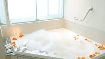Una bañera llena de burbujas y pétalos de rosa, con una ventana y un perchero a la vista.