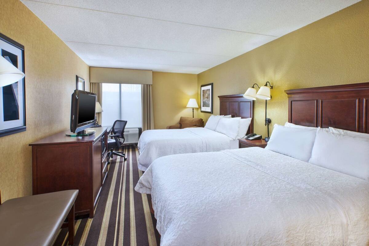 Une chambre d’hôtel avec deux lits, un bureau avec un ordinateur, une chaise, une télévision et une fenêtre avec des rideaux.