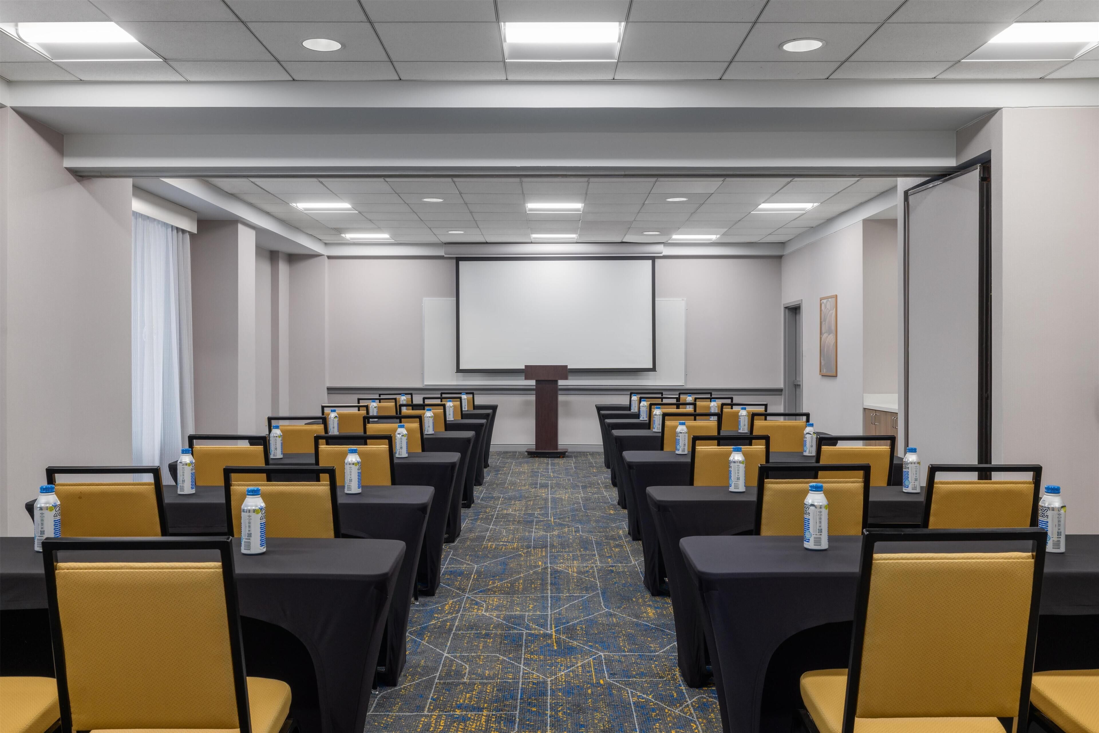 A conference room with rows of tables and chairs, a projector screen, and a podium.