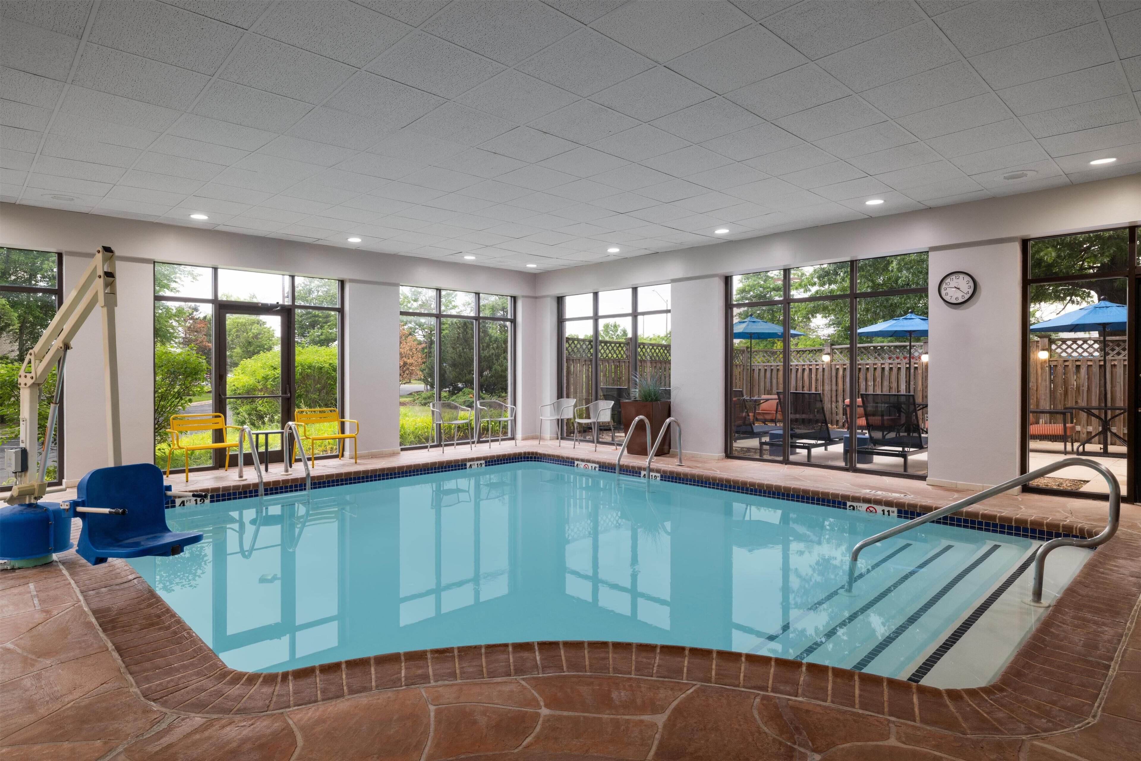 An indoor swimming pool with clear glass walls, a tiled floor, and a clock on the wall.