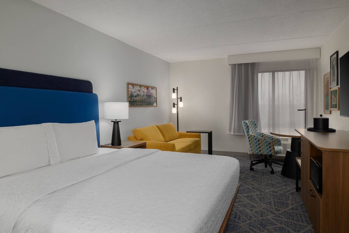 Une chambre d’hôtel avec un grand lit, un bureau, une chaise et une fenêtre avec des rideaux.
