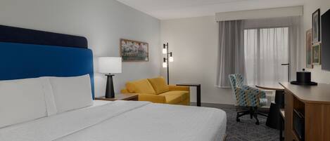 A hotel room with a large bed, a desk, a chair, and a window with curtains.