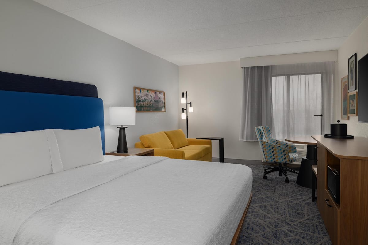 Une chambre d’hôtel avec un grand lit, un bureau, une chaise, une lampe et une fenêtre avec des rideaux.