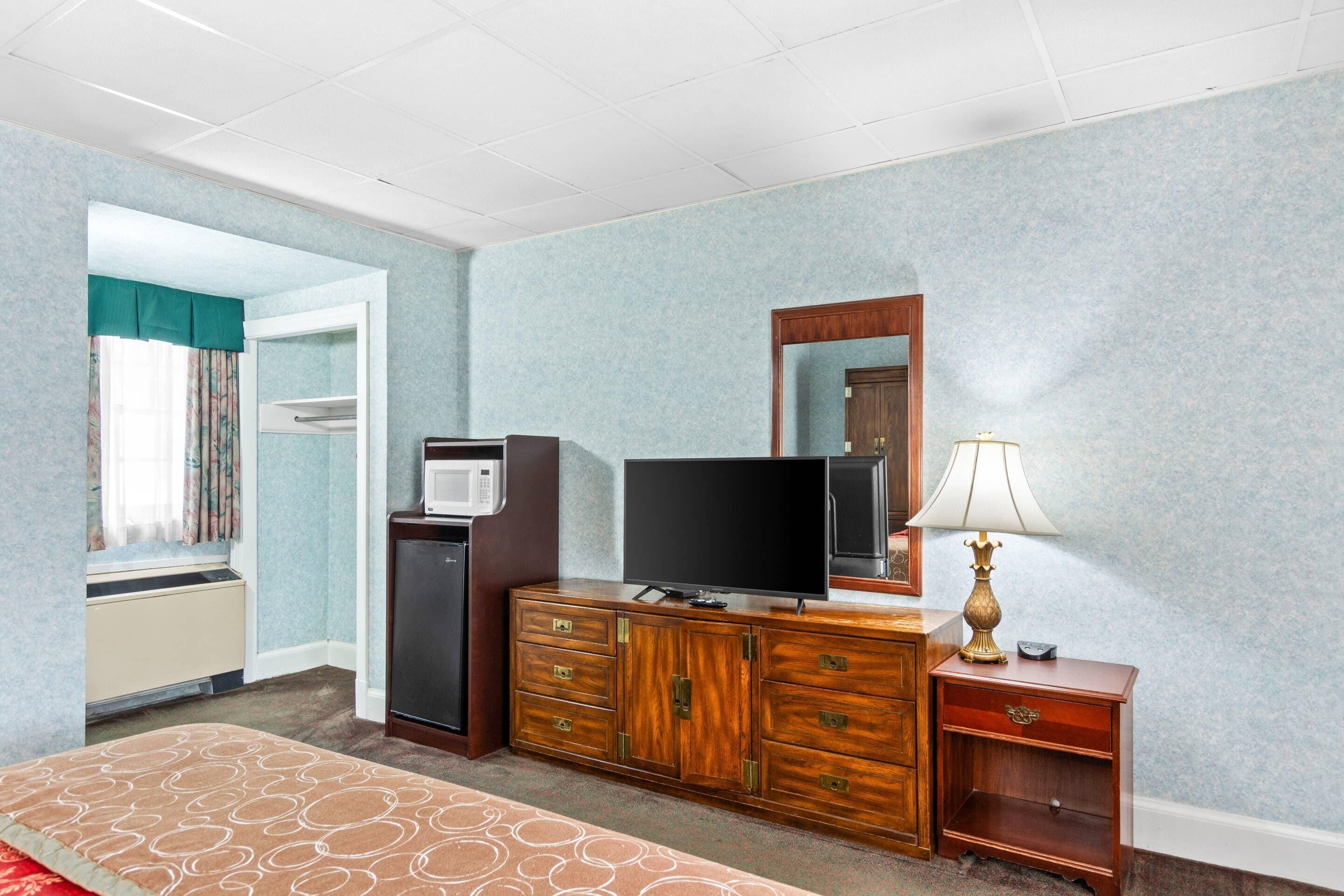 Ein Hotelzimmer mit einem Bett, einem Holzschrank, einem Fernseher, einer Lampe, einer Mikrowelle und einem kleinen Kühlschrank.
