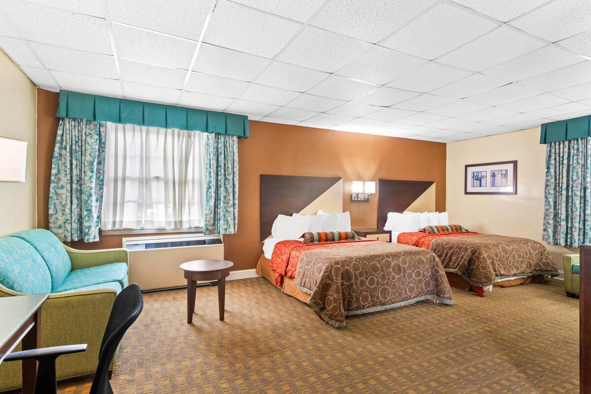 A hotel room with two beds, a sofa, a small table, and a window with curtains.