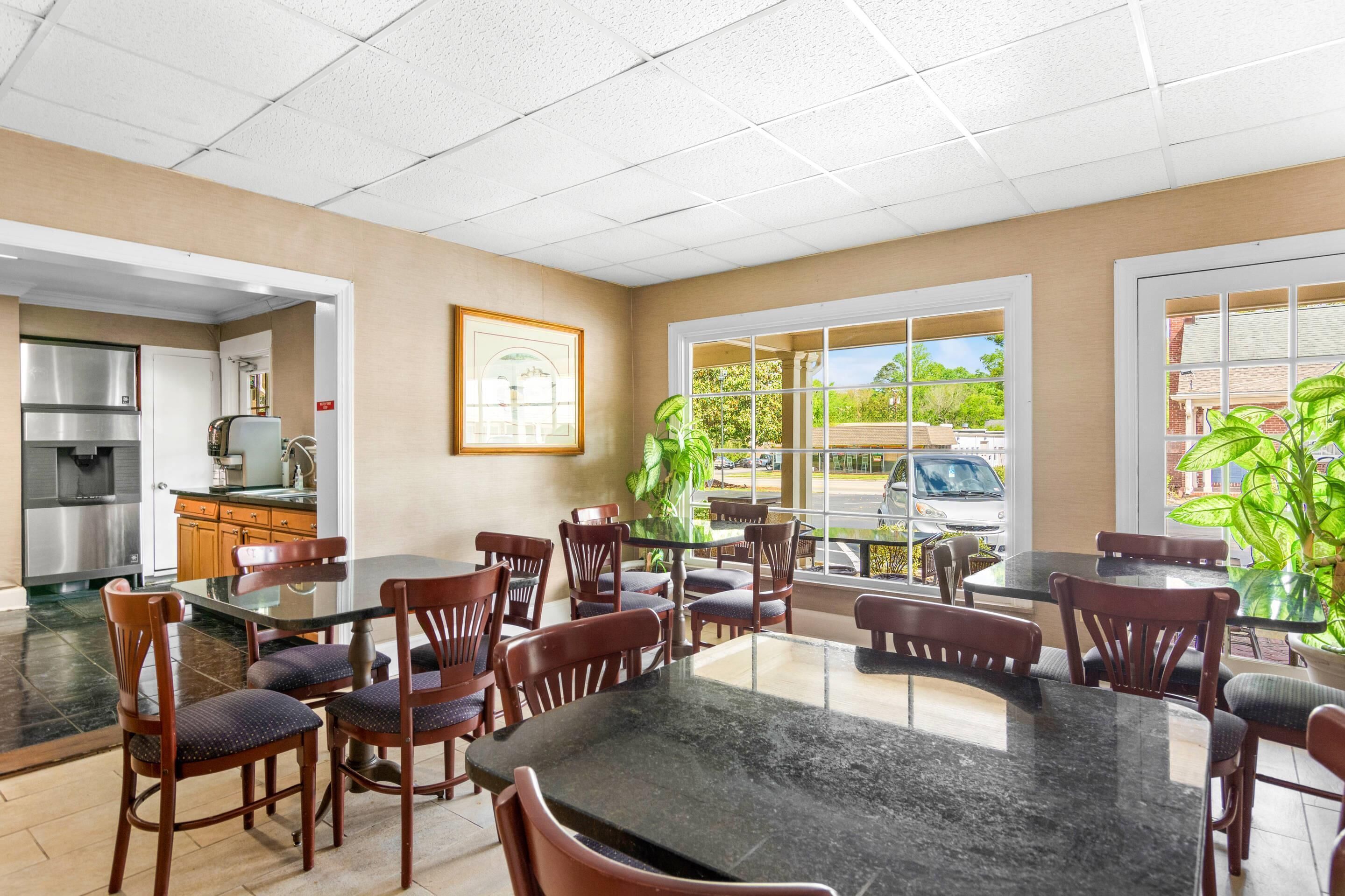 A spacious dining area with multiple tables and chairs, a kitchen area with stainless steel appliances, and large windows offering views of the outdoors.