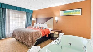 A hotel room with a large bed, a bathroom with a bathtub, and a painting on the wall. - Rodeway Inn Williamsburg Historic Area (Williamsburg)