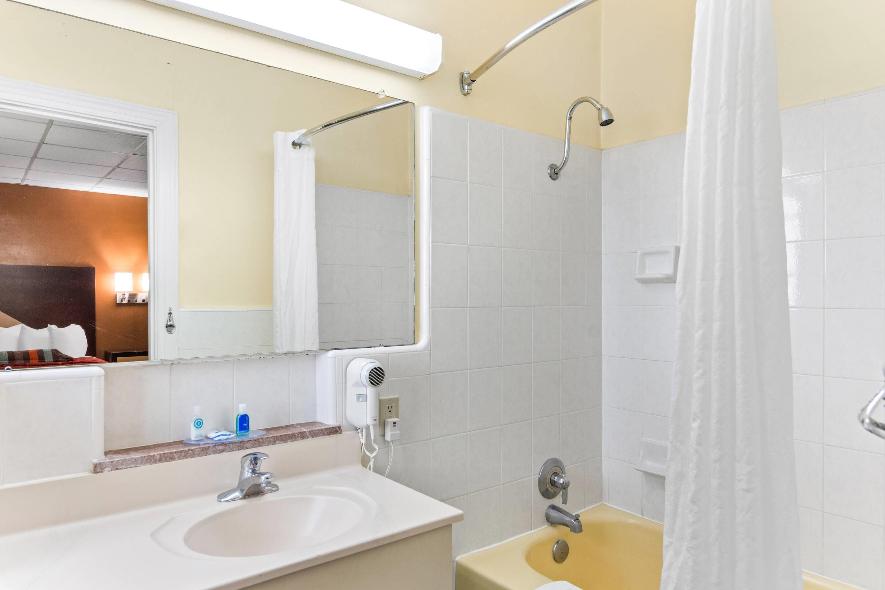 A bathroom with a sink, mirror, shower, and a towel rack.