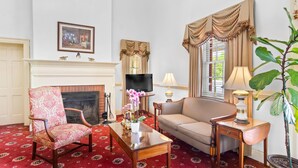 A well-furnished living room with a fireplace, a television, a sofa, a chair, and a large potted plant. - Rodeway Inn Williamsburg Historic Area (Williamsburg)