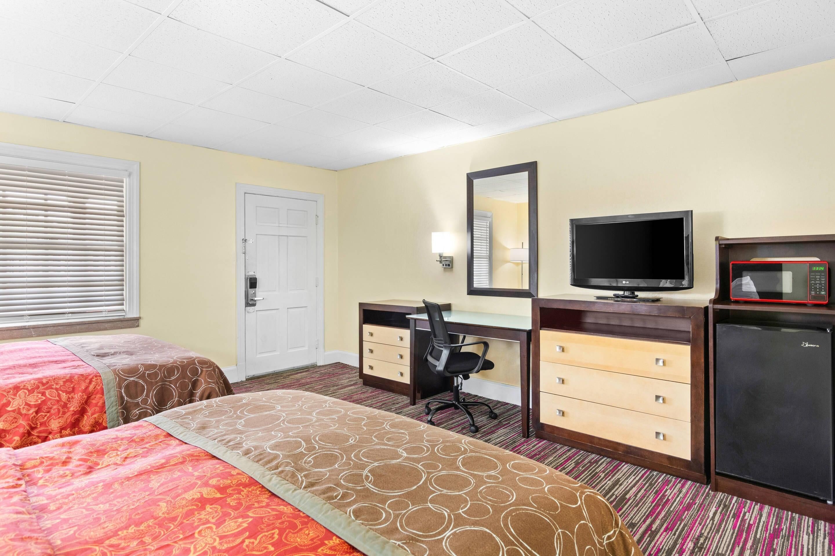 A hotel room with two beds, a desk with a chair, a television, a microwave, and a refrigerator.