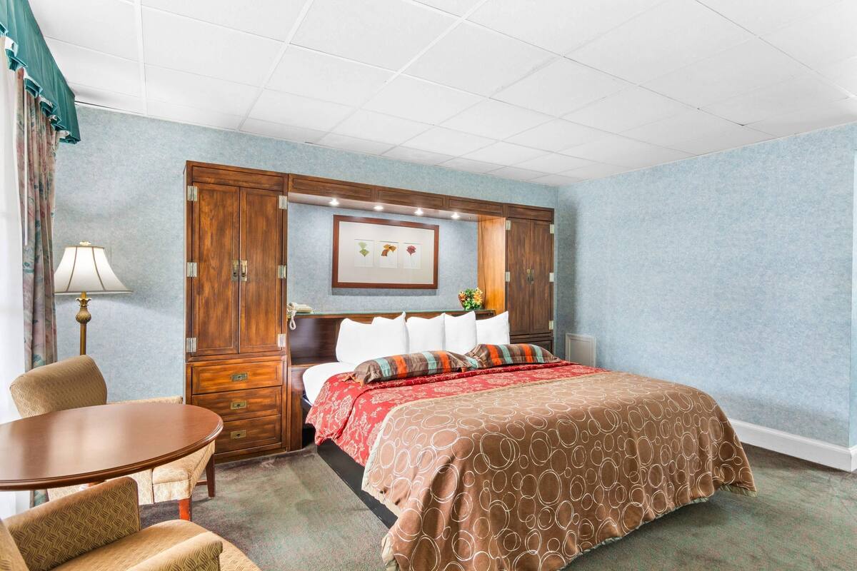 A hotel room with a bed, a wooden wardrobe, a desk, and a chair.