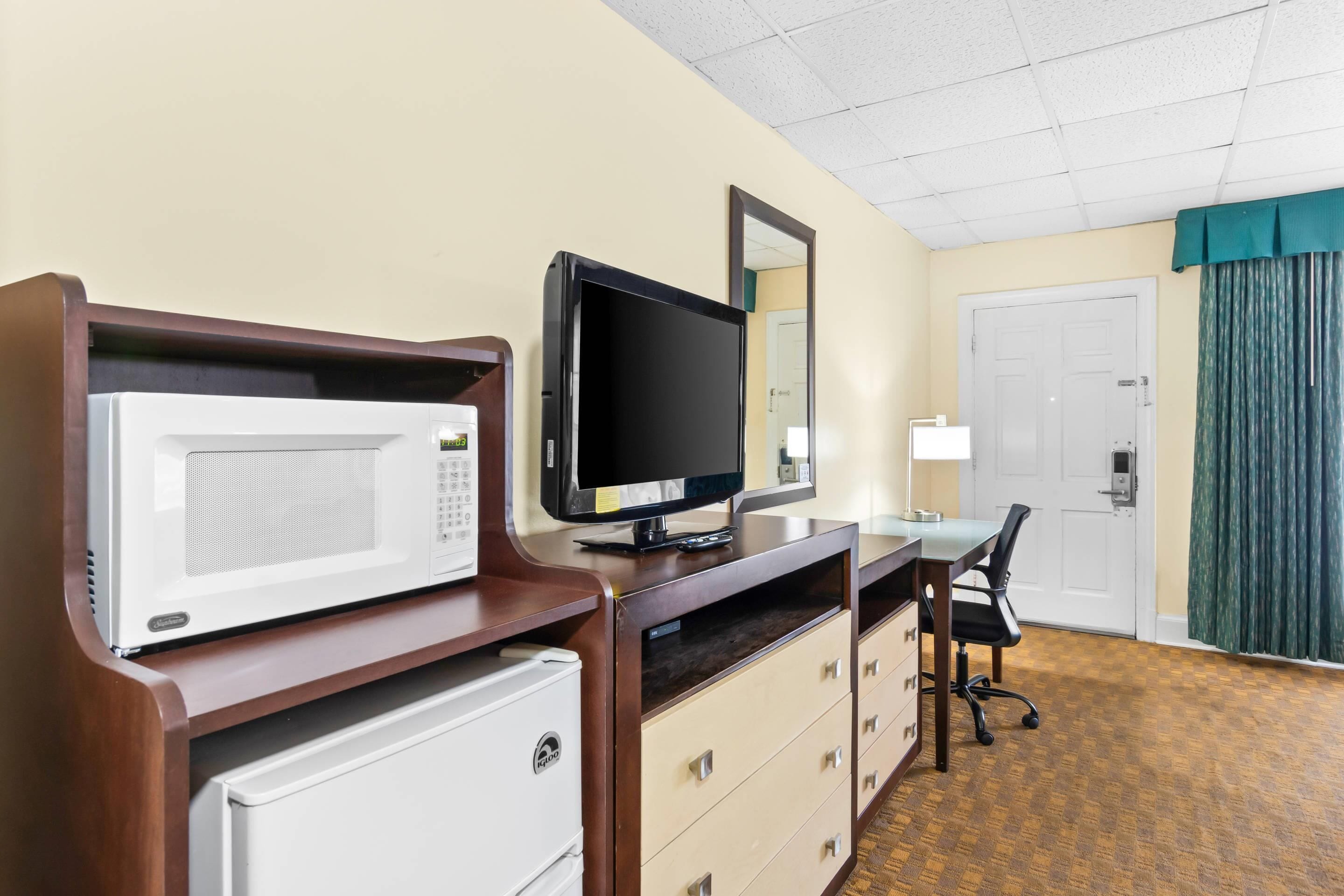 Habitación de hotel con microondas, televisor de pantalla plana, escritorio con silla, cómoda y puerta con cortina verde.