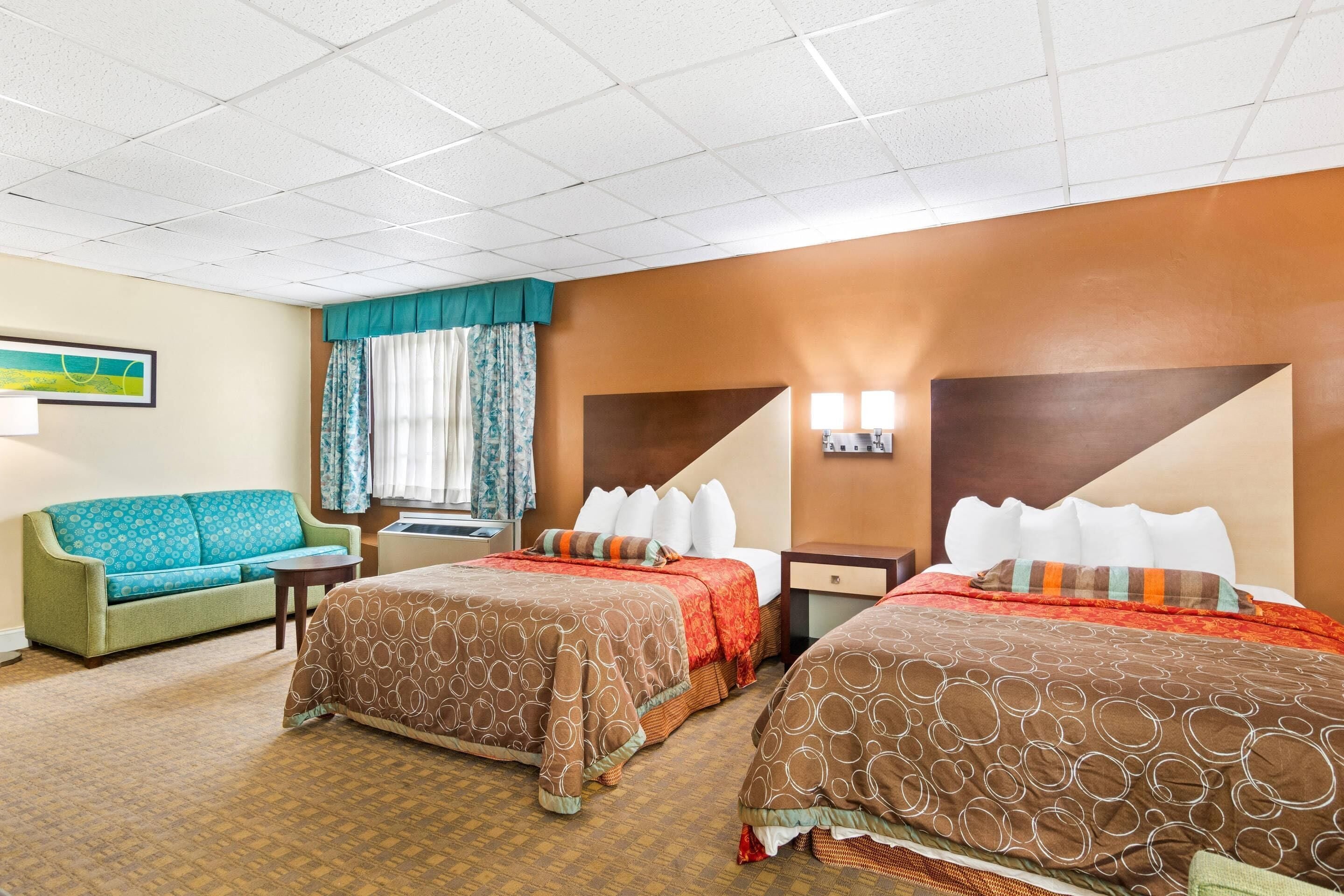 A hotel room with two beds, a sofa, a small table, and a window with curtains.