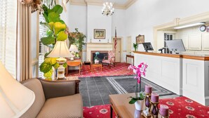 A hotel lobby with a fireplace, a reception desk, and a seating area with a sofa and armchairs. - Rodeway Inn Williamsburg Historic Area (Williamsburg)