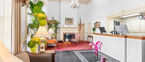 Um hall de hotel com lareira, balcão de recepção e área de estar com sofá e poltronas.
