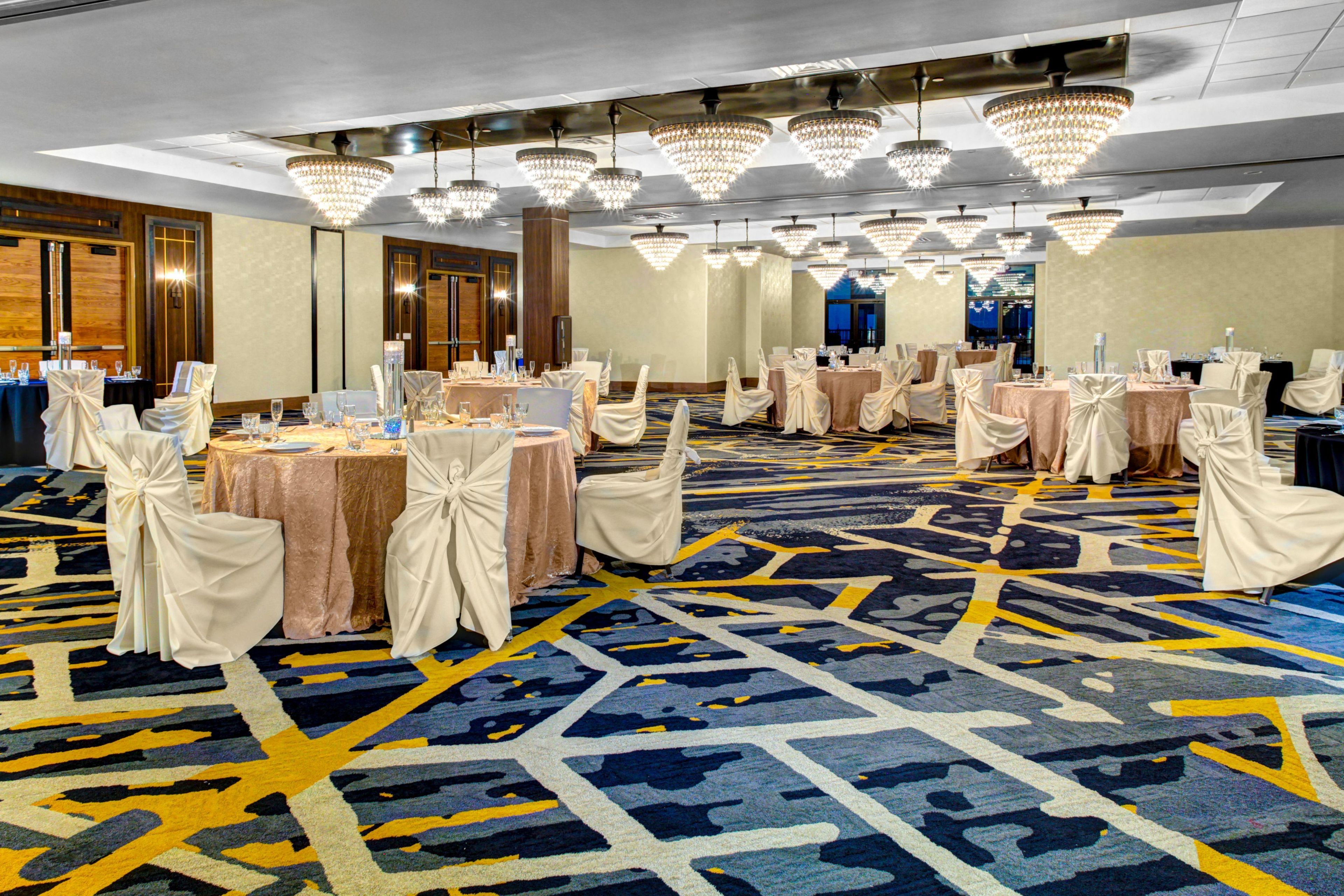 A banquet hall with round tables, chairs, and chandeliers.