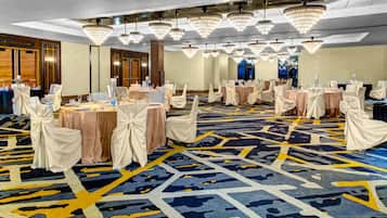 A banquet hall with round tables, chairs, and chandeliers.