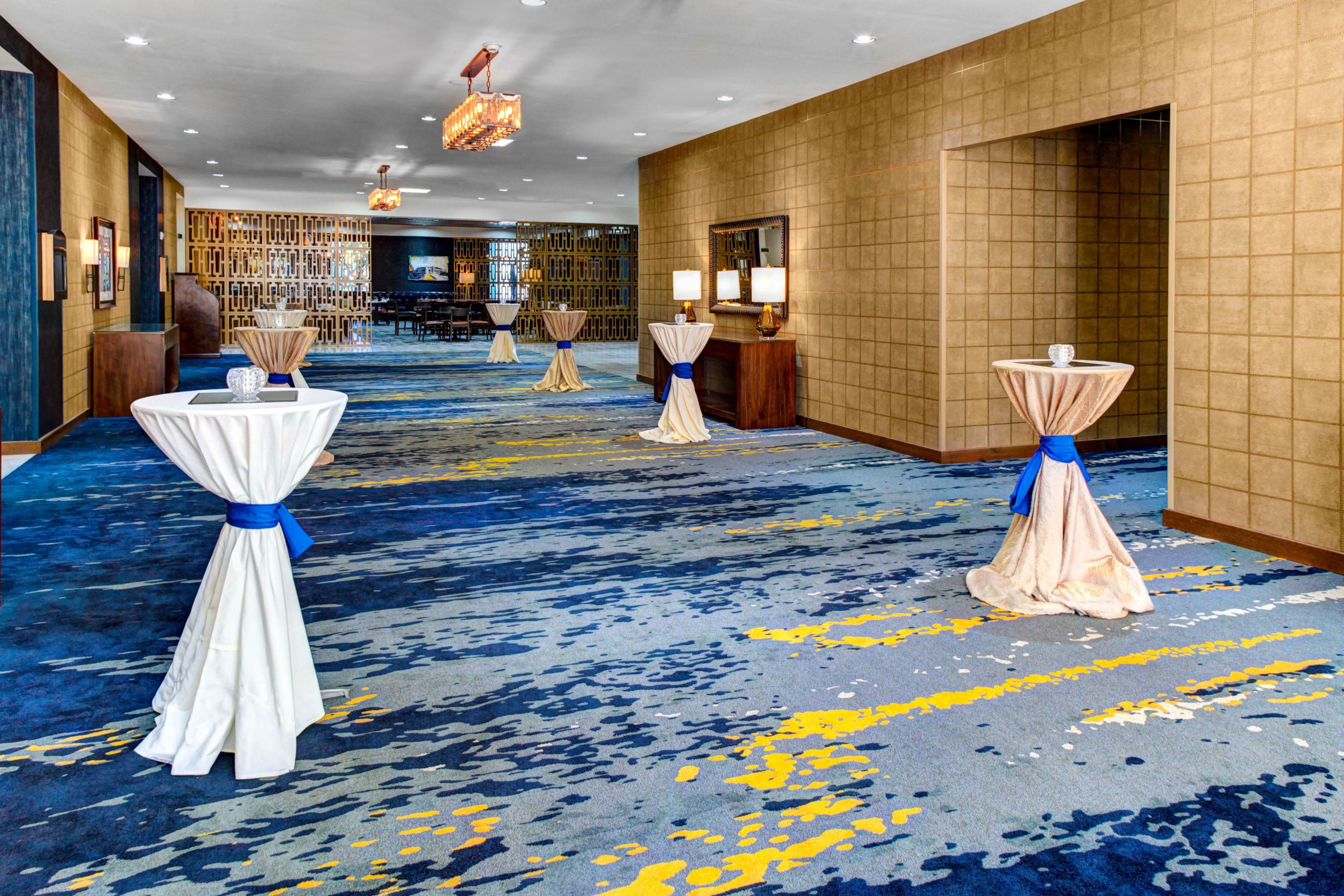 Eine Hotellobby mit blauem Teppich, Tischen mit weißen Tischdecken und blauen Bändern sowie einem Empfangsbereich.