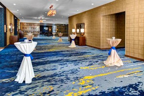 Eine Hotellobby mit blauem Teppich, Tischen mit weißen Tischdecken und blauen Bändern sowie einem Empfangsbereich.