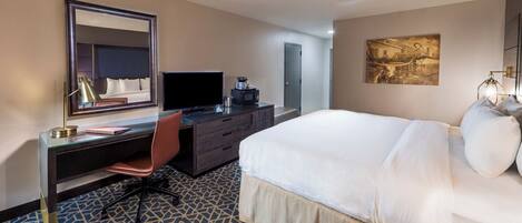 A hotel room with a bed, a desk with a computer, a chair, a dresser, and a large mirror.
