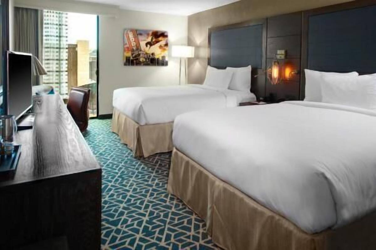 A hotel room with two beds, a desk, a lamp, and a painting on the wall.